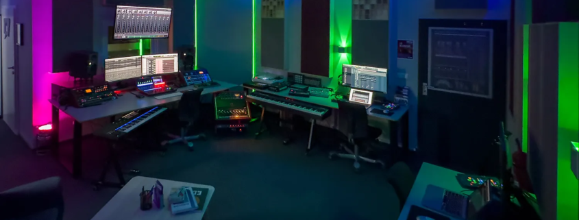 Modernes Tonstudio mit farbiger indirekter Beleuchtung, ausgestattet mit professioneller Audio-Technik.